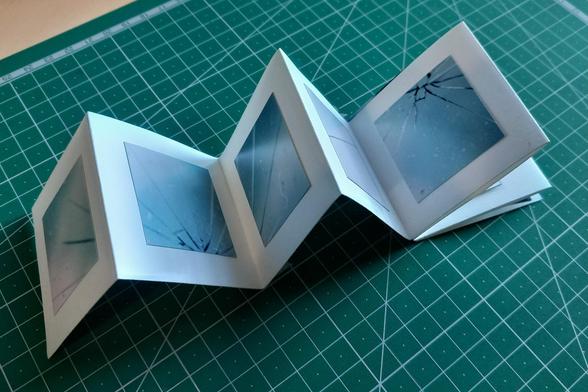 Leporello petit format : photo d'un éclat sur une vitre sur fond de ciel orageux, découpée et collée sur du papier de récup. Sur la face non visible ici il y a une petite broderie au points de croix extrait de ma série "Fragment de fantôme".