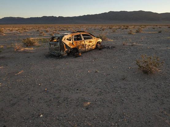 Burnt shell of abandoned car in desert landscape.