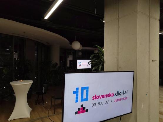 Záber z priestorov The Spot v Bratislave, kde sa čoskoro začne oslava 10. narodenín o.z. Slovensko.Digital
v zábere je stĺp, stolček a dve obrazovky s nápisom:
10 slovensko.digital
od núl až k jednotkám