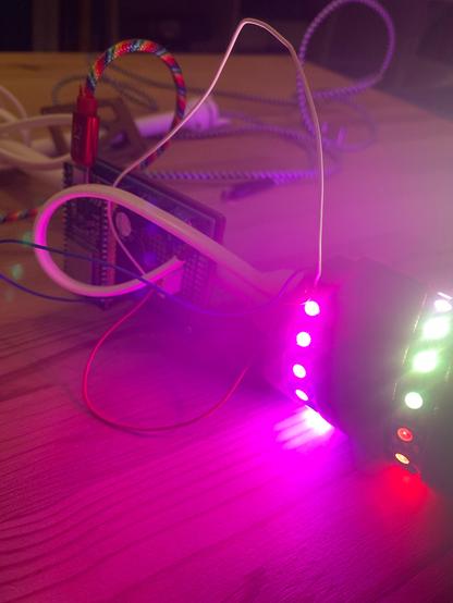 An ESP32, a mess of cables and pink leds in a spiral shape are on a table