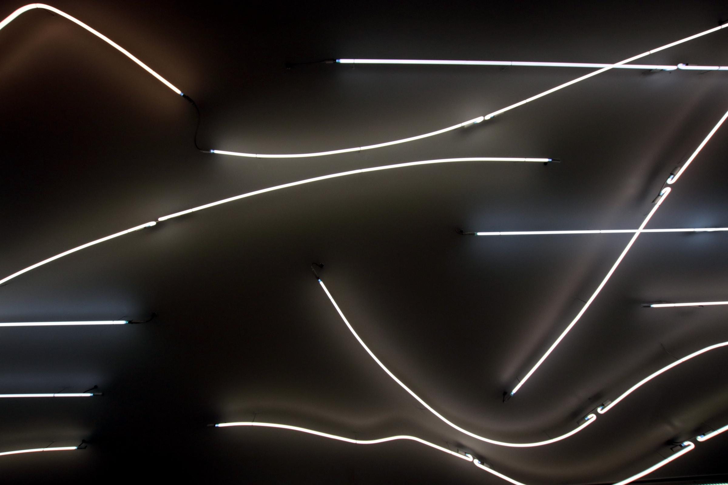 Das Bild zeigt die Decke einer U-Bahnstation in Stockholm. An der Decke sind kunstvoll gebogene, weiße Leuchtstoffröhren angebracht.