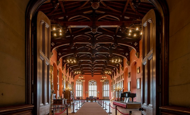 a photo of one of the halls, the ceiling is a really beautiful design done in wood, chandeliers glowing softly, light coming in the big windows at the end of the hall 