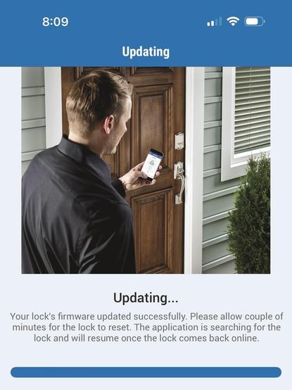 A man stands outside the front door of a house holding a phone, installing a firmware update.