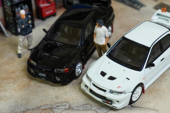 Two cars of Mitsubishi Lancer RS Evolution.
One is Evolution 6, Monte Carlo Edition, Scortia White and one is Evolution 5, Pyrenees Black. 
Both by Hobby Japan in 1:64 scale with 1:64 figures on AREA 164.