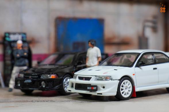 Two cars of Mitsubishi Lancer RS Evolution.
One is Evolution 6, Monte Carlo Edition, Scortia White and one is Evolution 5, Pyrenees Black. 
Both by Hobby Japan in 1:64 scale with 1:64 figures on AREA 164.