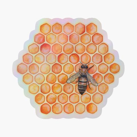 Sticker holographique hexagonal d'une aquarelle représentant une abeille au milieu d'alvéoles remplies de miel.