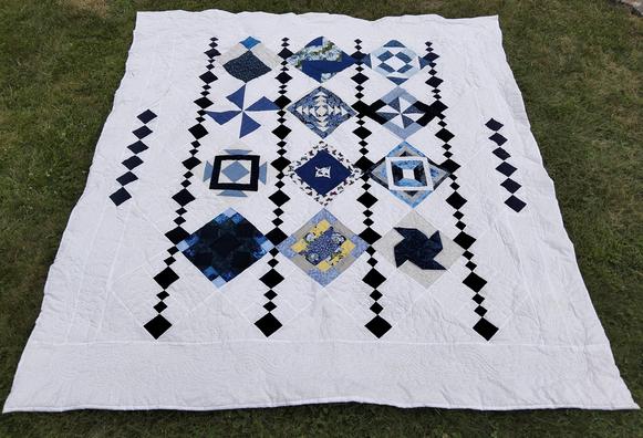 a quilt, it is shapes coming dowwn in vertical rows against a white background, the shapes are mostly dark blue , some light tan yellows 