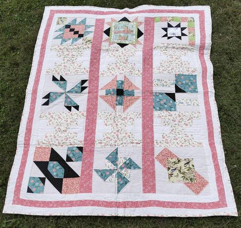  a quilt, it is pink and floral patterns, blue as well and light naples yellow and some black, a thin pink border around it with a thin white border around that, columns of pink rising up vertically