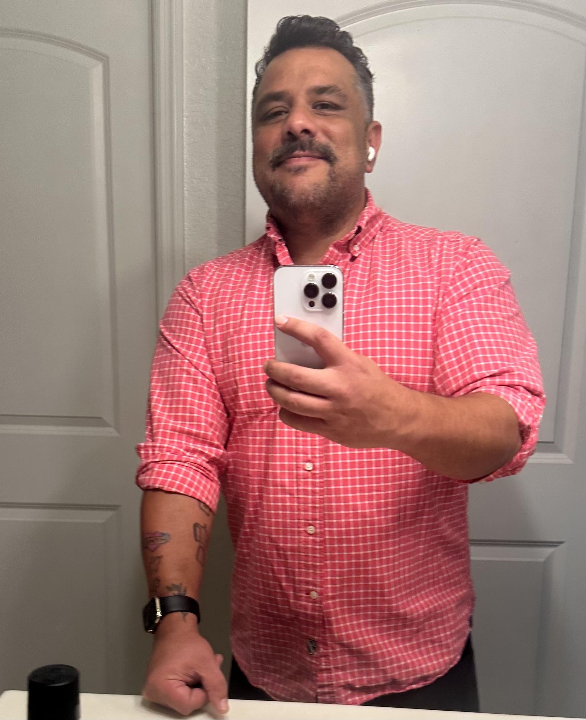 Me, a selfie in a bathroom mirror. I'm wearing a red-ish checkered button up shirt.