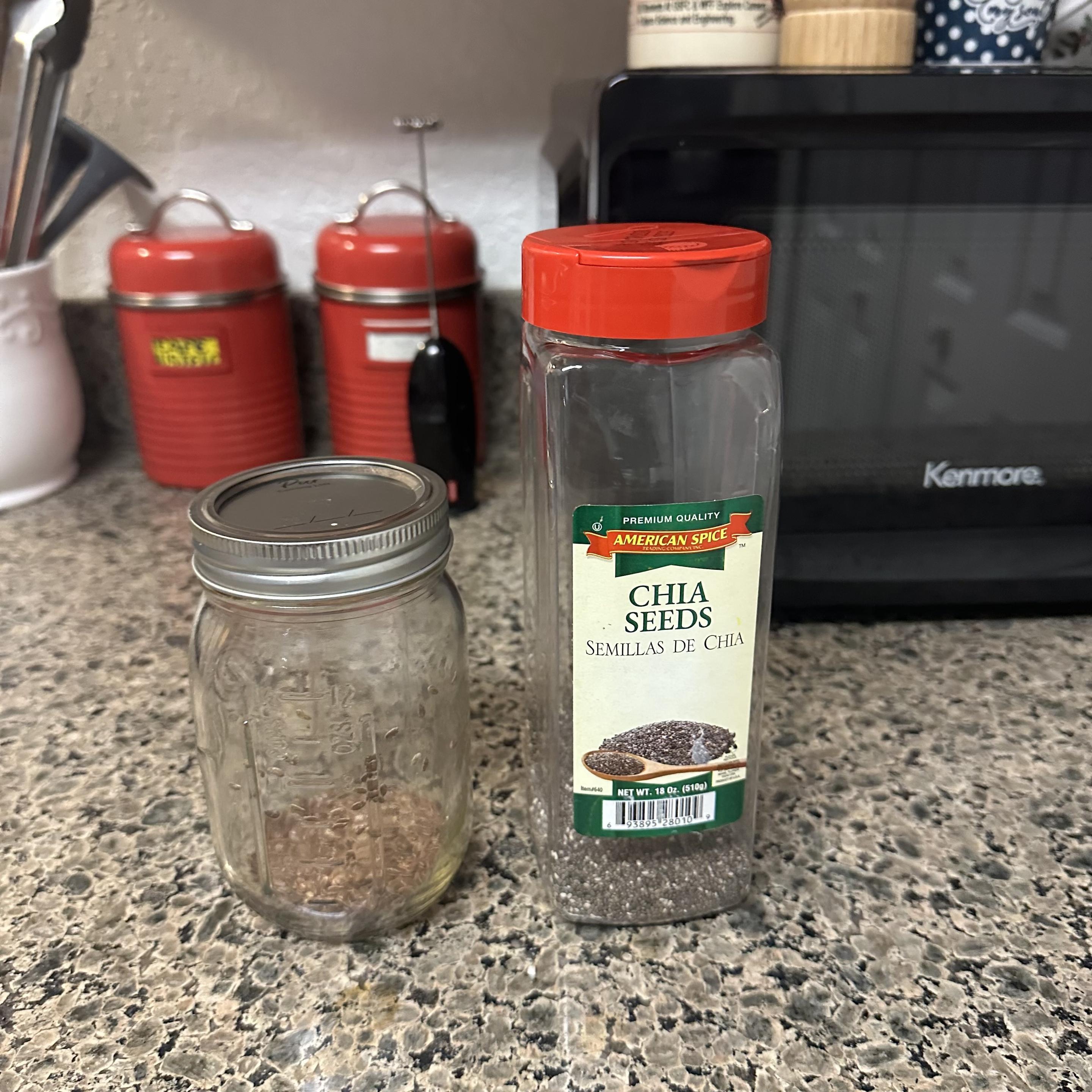 A countertop featuring a glass jar with a metal lid with flax seeds and a container of chia seeds. In the background, two red canisters and a black microwave are visible.