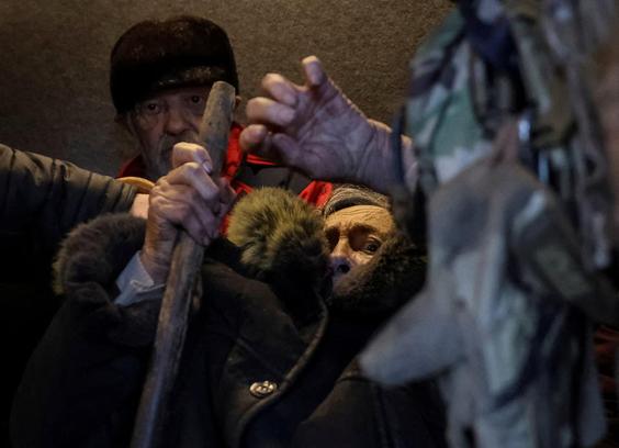 A terrified old woman holding a stick raises her other hand.
