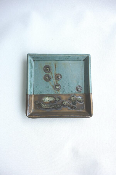 Gleiche Grundform, 1/3 ist goldbraun und 2/3 türkis mit Kreisen in der anderen Farbe