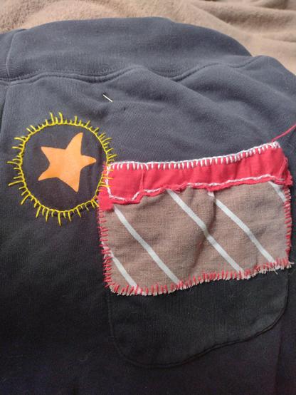 Foto van een deel van een zwarte joggingbroek met stukjes kleurige stof en borduurwerk die de gaten bedekken.