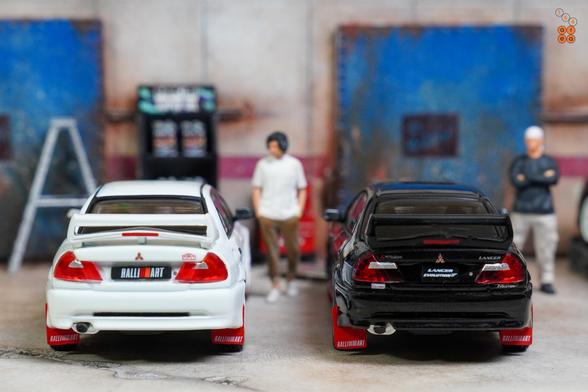 Two cars of Mitsubishi Lancer RS Evolution.
One is Evolution 6, Monte Carlo Edition, Scortia White and one is Evolution 5, Pyrenees Black. 
Both by Hobby Japan in 1:64 scale with 1:64 figures on AREA 164.
