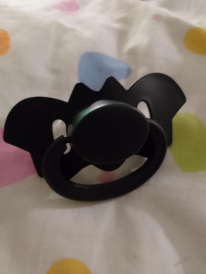 Black bat shaped adult pacifier on a multicoloured heart bedspread. 