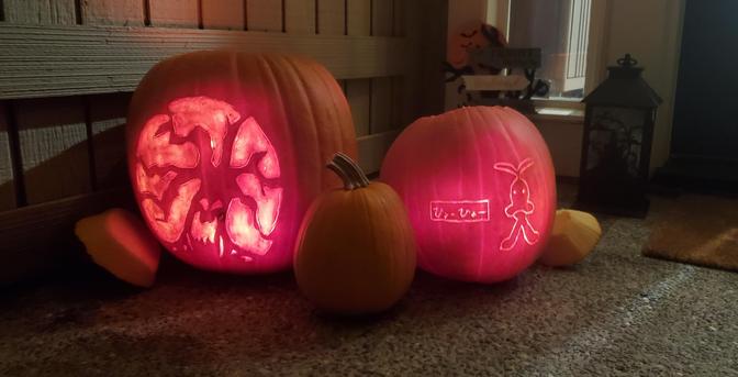 Two jackolanterns on a door step with a pumpkin in the middle.