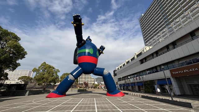 giant life size statue of a mecha/robot - Tetsujin 28 / Gigantor - standing in a public square, lit fully by the sun, blue cloudy sky behind it