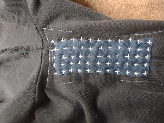 Een zwarte joggingbroek met donkerblauwe patch met daarop sashiko borduurwerk in de vorm van rijen met witte kruisjes.