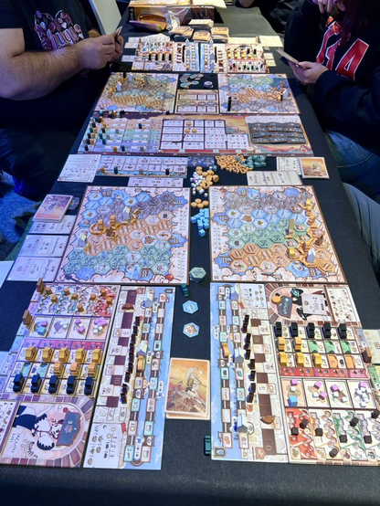 Foto del despliegue para una partida al juego Sweet Lands con 4 jugadores que, en este caso, a necesitado de 2 mesas para los tables personales, las cartas y el tablero principal.