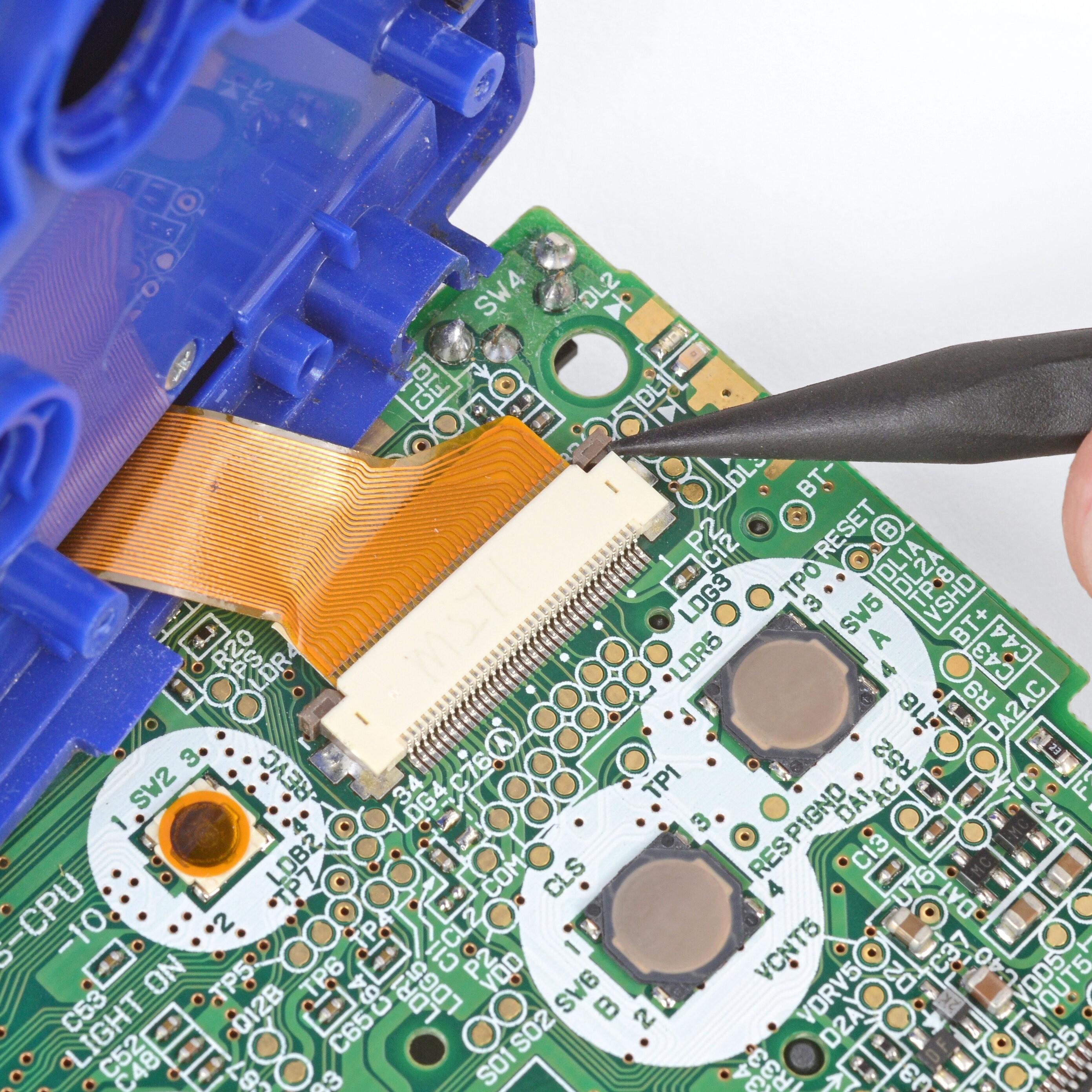 Close-up view of a Game Boy Advance SP circuit board as someone uses a black spudger to pry the connector for the ribbon cable attaching the motherboard to the blue screen assembly.