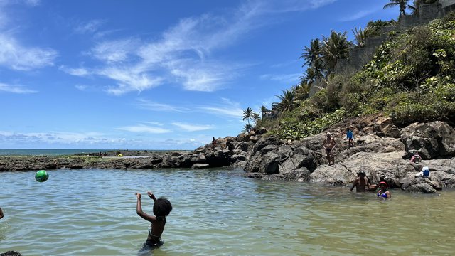 Un océano de mar transparente, es como una piscina entre rocas , se ve un niño y una pelota