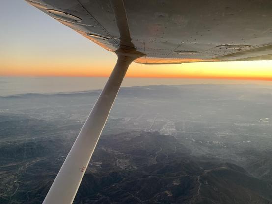 Sunset over a hazy city and cloudy sea, seen from the air below the wing of an airplane