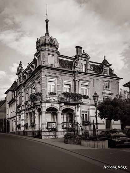 Das historische Haus Sachs in Schotten im Vogelsberg, einst Druckerei Engel. Ein prachtvolles Gebäude im Stil des Historismus mit Zwiebelturm, verziertem Erker und schmiedeeisernem Geländer. In Sepia fotografiert, wirkt es wie eine Erinnerung an vergangene Zeiten.