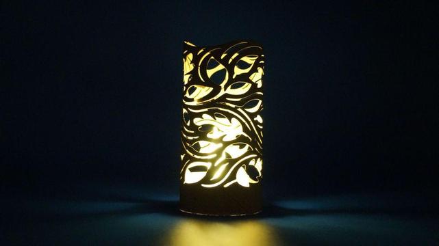 Zylindrische Laterne aus einer Klopapierrolle mit herbstlichem Wirbelmuster, durch das warmes LED-Licht scheint.