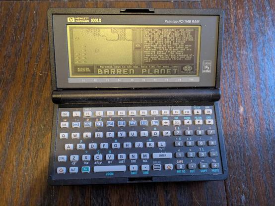 A photograph of a Hewlett Packard 100LX running the downloadable Barren Planet campaign Waterworld, showing the Nuvutech briefing for the first mission.