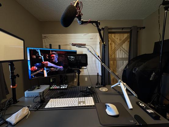 Setup in a small video studio with camera and teleprompter iPhone and Mac Mini on a table, as well as a microphone on a boom stand, light, and an ATEM switcher.
