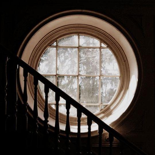 An old-fashioned staircase balustrade in front of a round window.