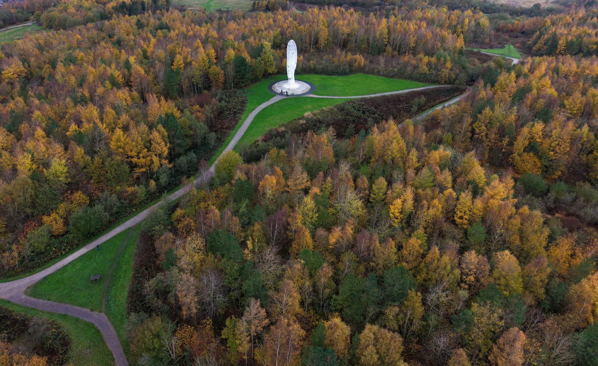 A drone view of the Dream Sculpture surrounded by trees displaying their Autumn colors near Saint Helens, Britain.