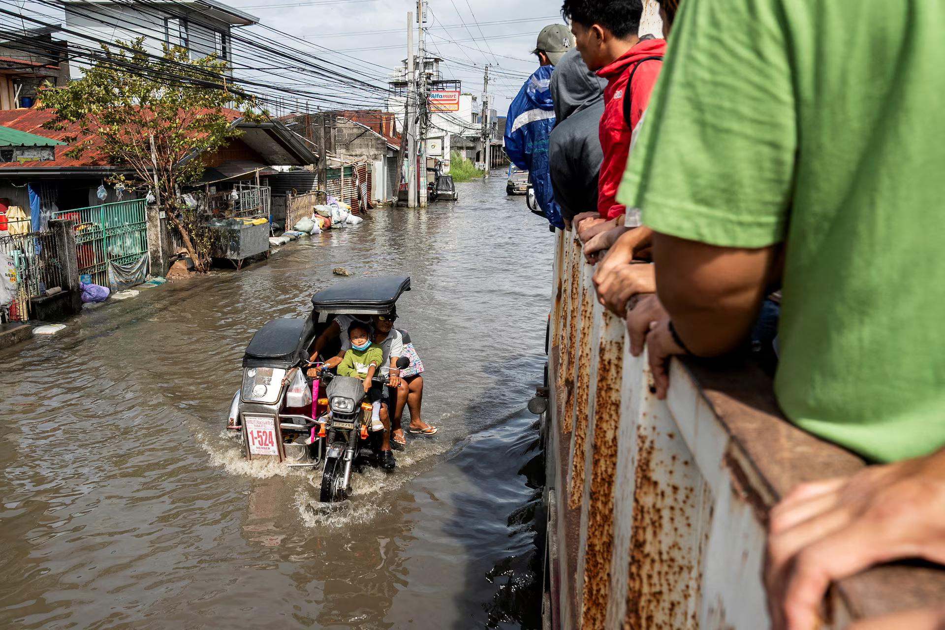 People ride a motorbike with a sidecar as it wades through a flooded road following flooding brought by high tide and Super Typhoon Fung-wong, in Macabebe town.