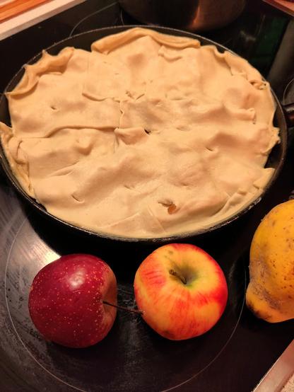And, off to the oven...

A pan filled with apples covered with pastry, next to it 2 apples and quince.