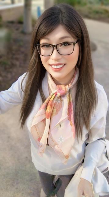 Stellar is smiling, wearing a light-colored sweater and a soft pink floral scarf. The background shows a pathway and greenery, giving casual vibe.