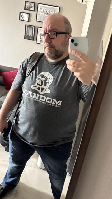 mirror selfie of me in my hotel room wearing my MANDOM tshirt - white stylised illustration of a roman-looking head and neck, big text with slab serifs MANDOM, and in helvetica underneath the strapline "all the world loves a lover. all the world loves MANDOM"