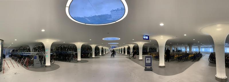 Panoramic view of a large space filled with bicycle racks, the ceiling of which is supported by pillars.