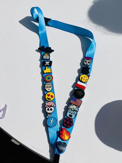 Bright blue lanyard laid flat with colorful enamel pins, including skulls, emoji faces, flags, WWDC Scholar badge, and a silver heart.