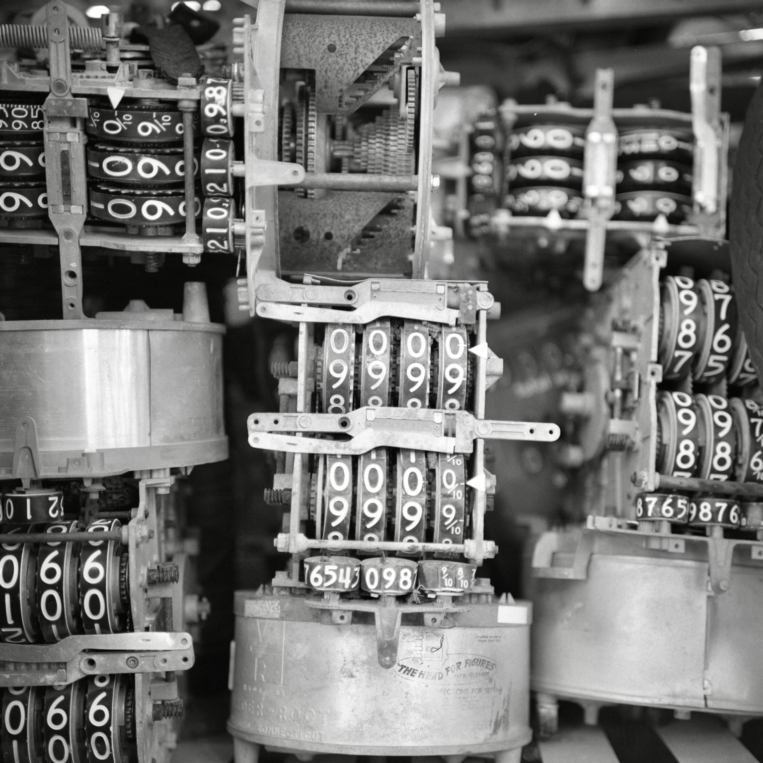 A black-and-white film photo. Very old gasoline registers, that fit inside of fuel pumps, sit collected in a box at Broadway Paul’s Antiques & Salvage in Paige, Texas. Friday, November 7, 2025.