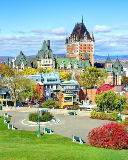A stunning view of the Fairmont Le Château Frontenac in Quebec City, Canada, from a park with vibrant autumn foliage.
