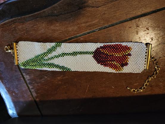 A brick stitch beadwork bracelet on a cream base of a red tulip