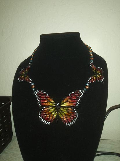 A peyote stitch necklace with a large monarch in the center and two smaller monarchs to either side. They are connected by a chain or orange and blue flowers