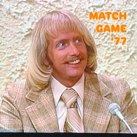 A man with straight blond shoulder-length seemingly permed hair with an impeccable inward flip at the ends waits to speak on a popcorn-ceiling-backed set in 1977. 