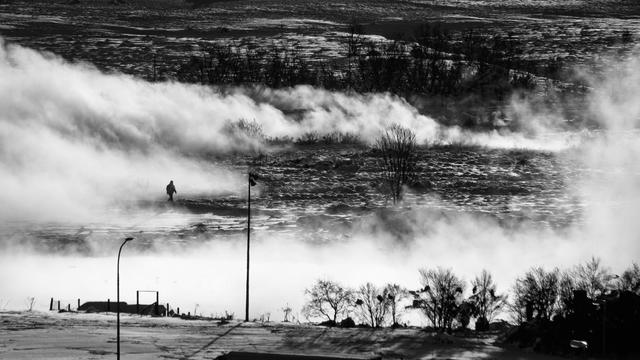 Black and white picture of a person walking in a swamp land surrounded by a steam coming out of the ground.
