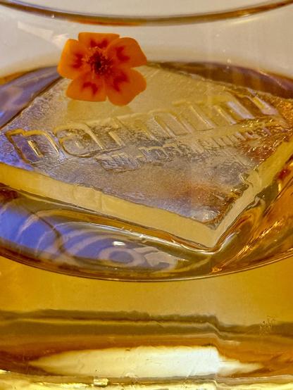 A closeup on an ice cube with the bar name embossed in it and a tiny flower on top