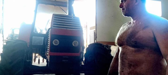 Hombre grande de campo al lado de un tractor, mirándole