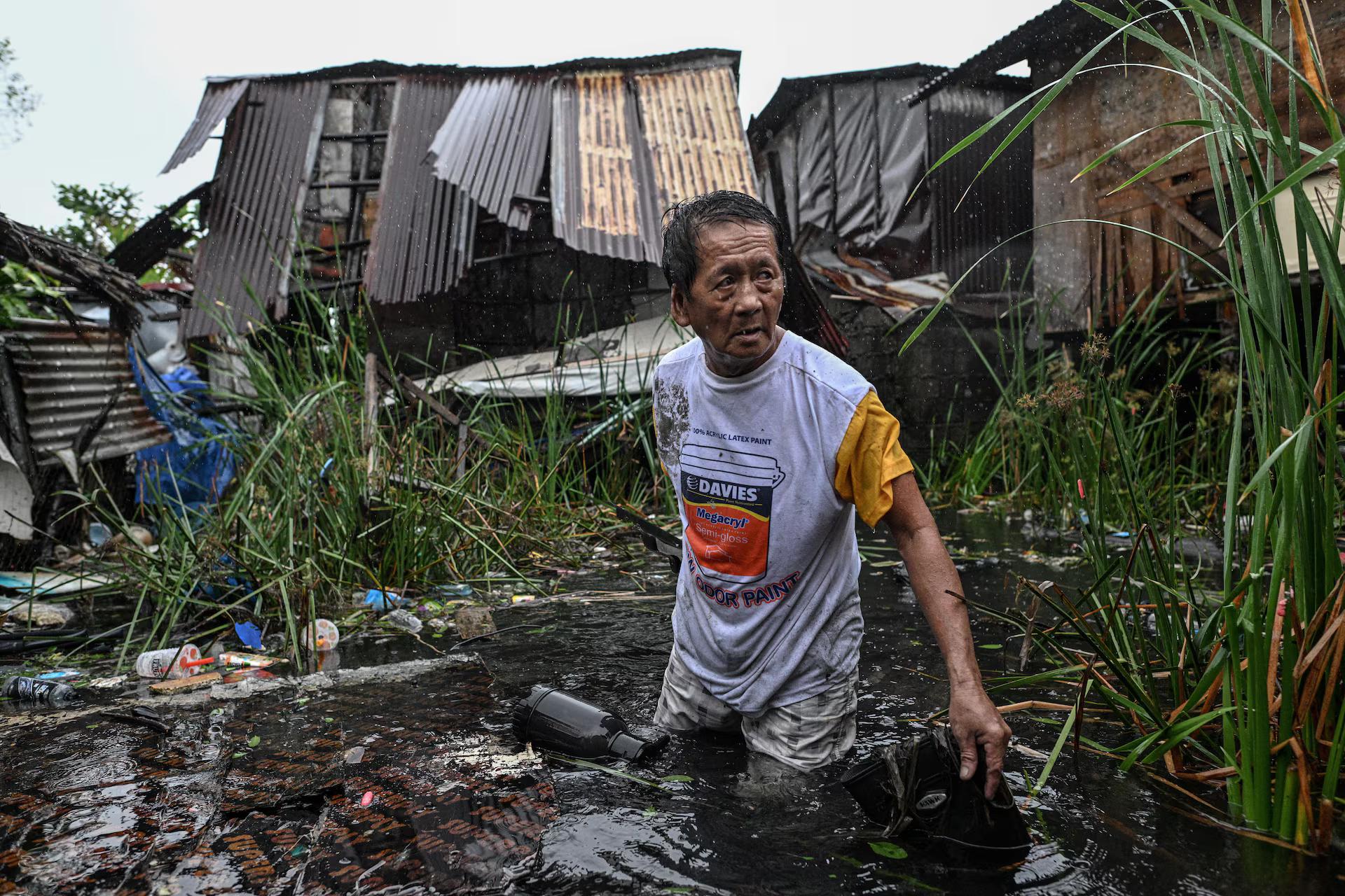 A man wades through the flood as he recovers a roof blown from his house due to strong winds.