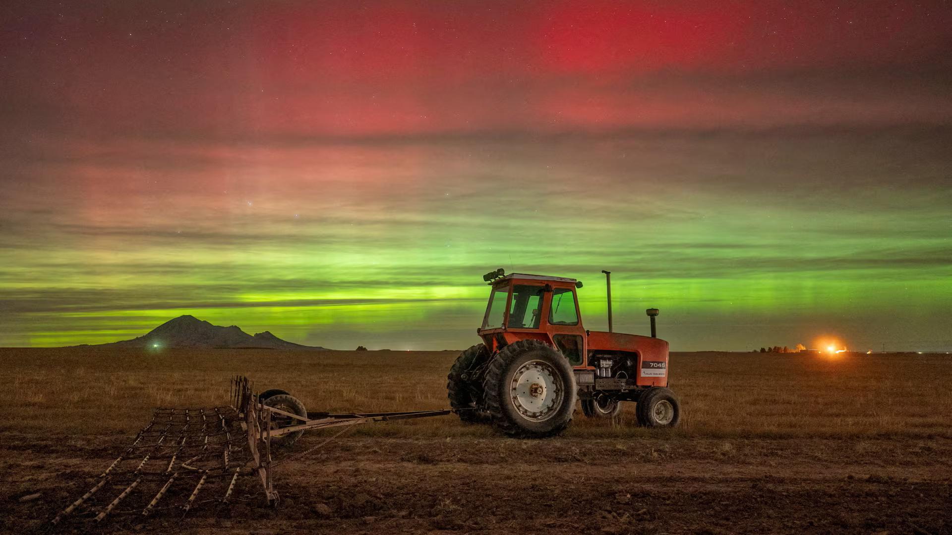 A red & green aurora over a tractor in a field.