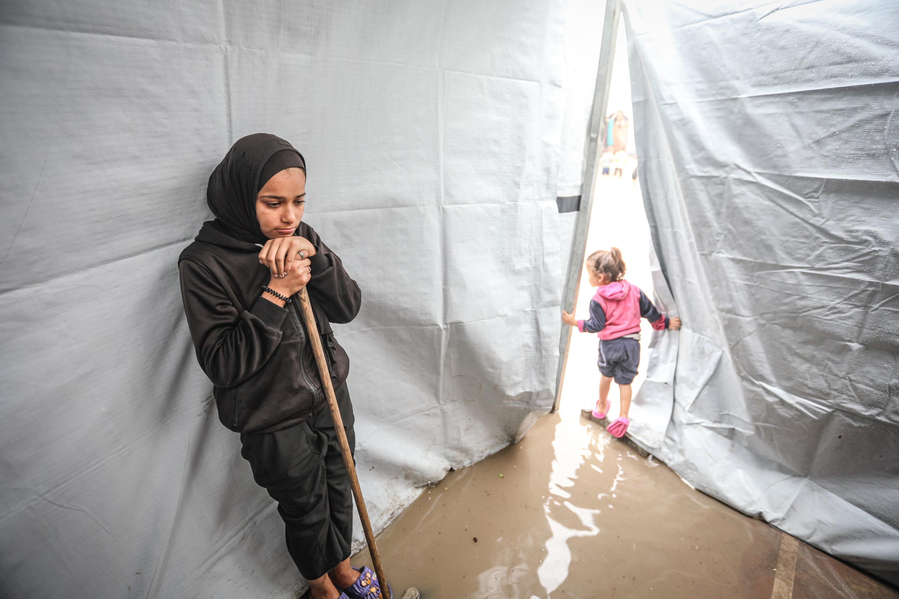 A young woman tries to remove the water after their makeshift tent flooded with intense rain.