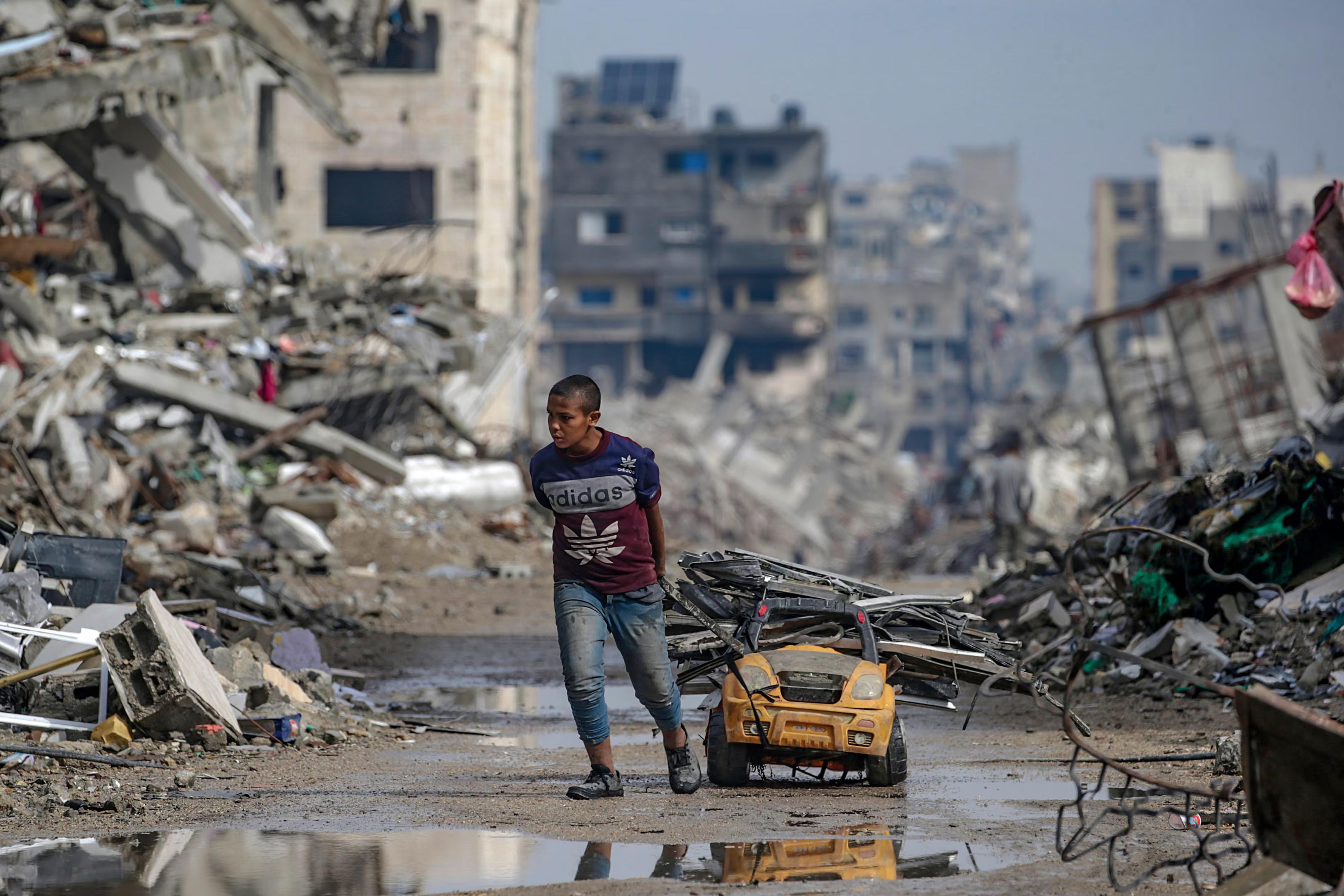 A Palestinian boy collects scrap metal from a street filled with debris.